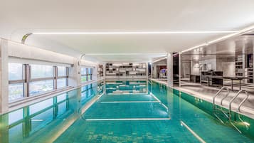 Ein Schwimmbecken mit klarem Wasser, umgeben von einem modernen Innenraum mit Glaswänden und Metallgeländern.
