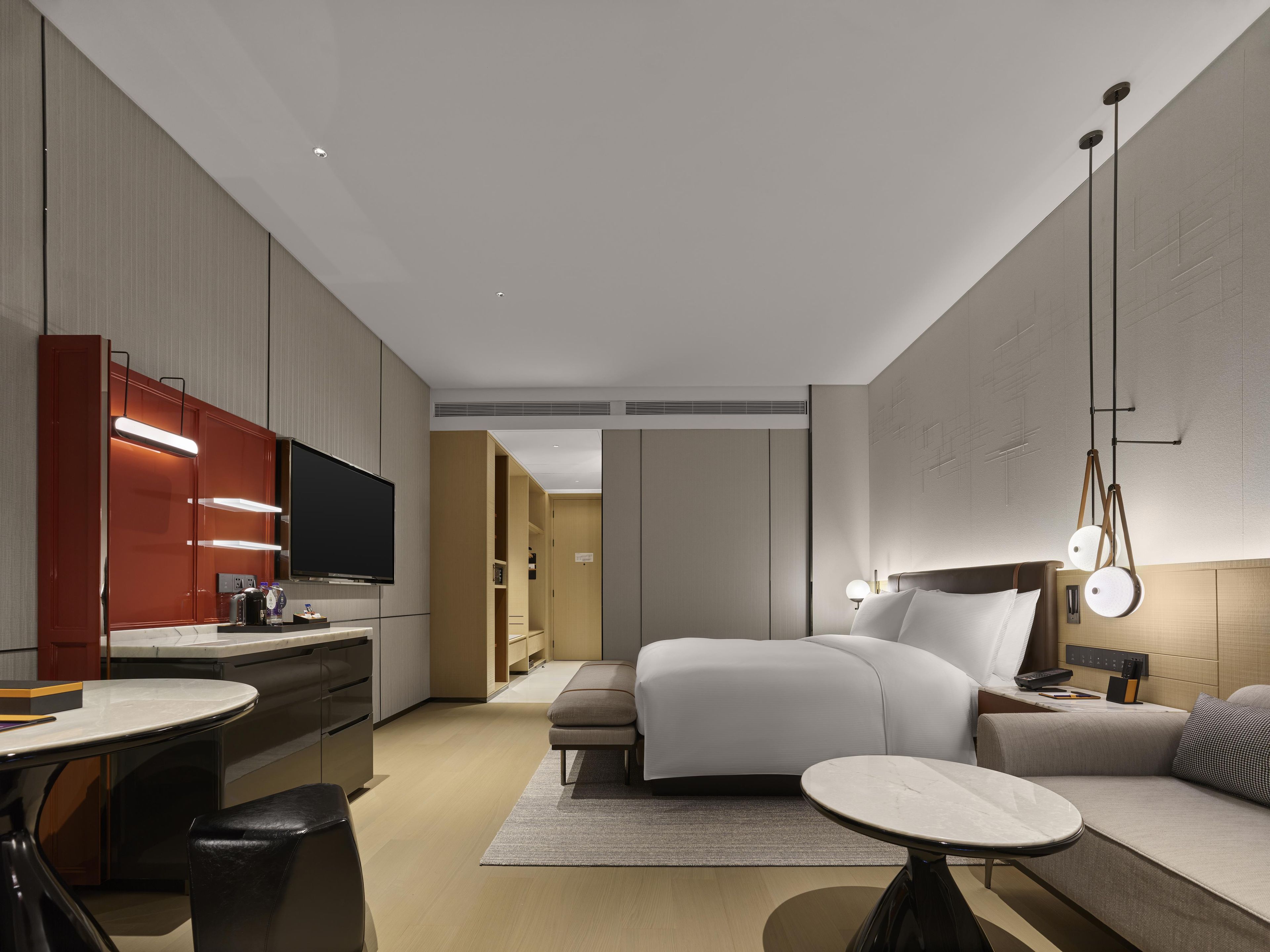 Una habitación de hotel moderna con cama, mesita de noche y una zona de estar con sofá y sillones.