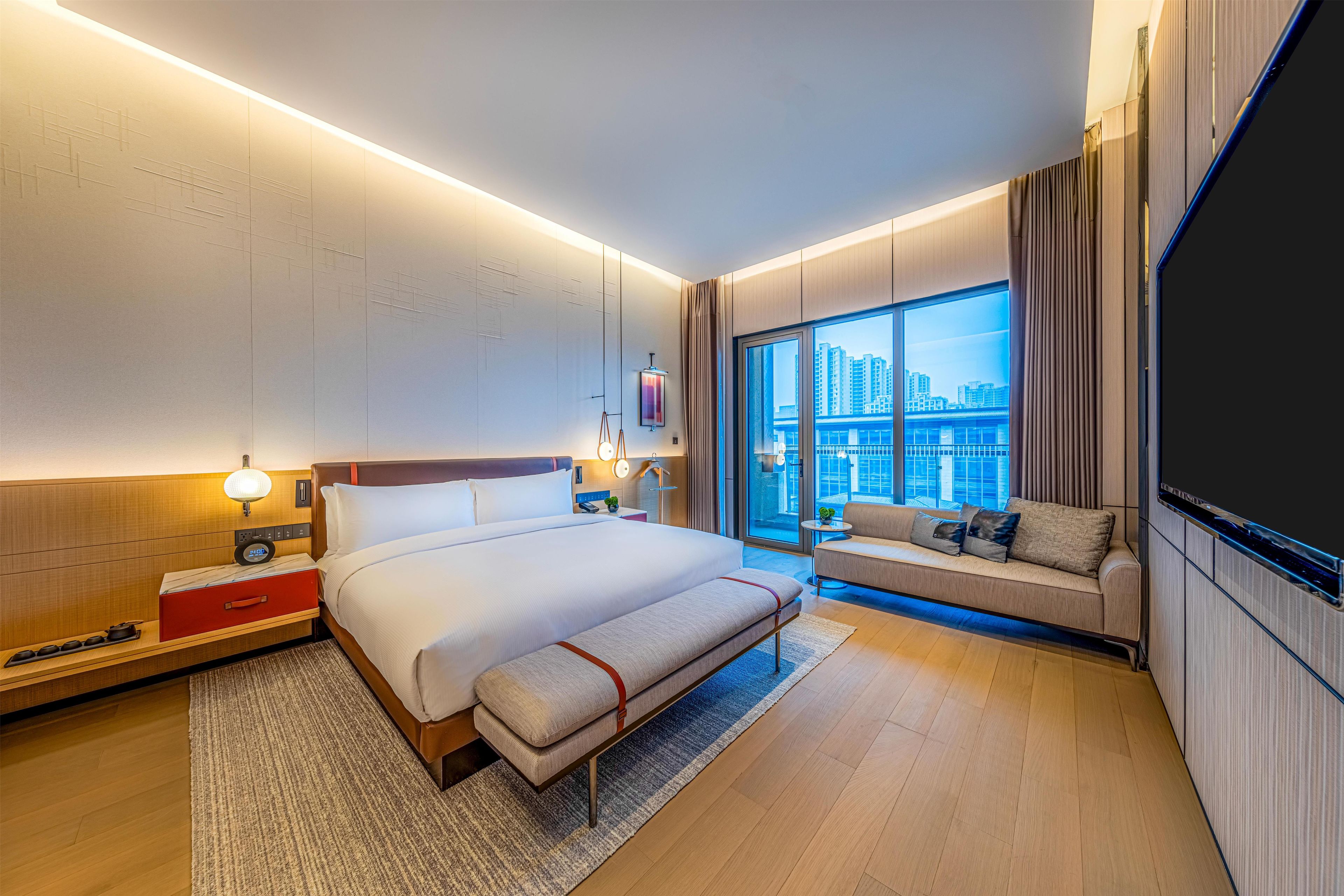Una habitación de hotel moderna con una cama grande, una zona de estar, un televisor y vistas a la ciudad.
