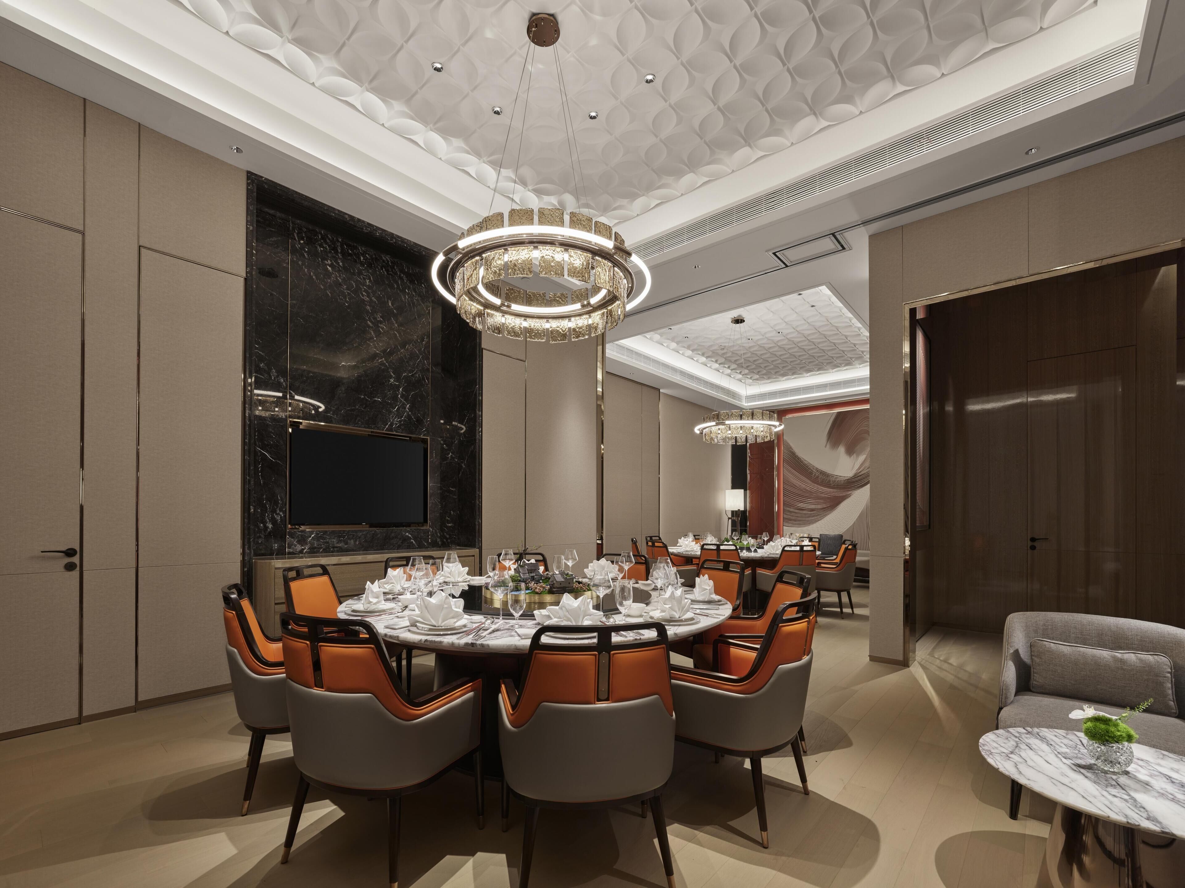 A dining area with a round table, chairs, a chandelier, and a television on the wall.