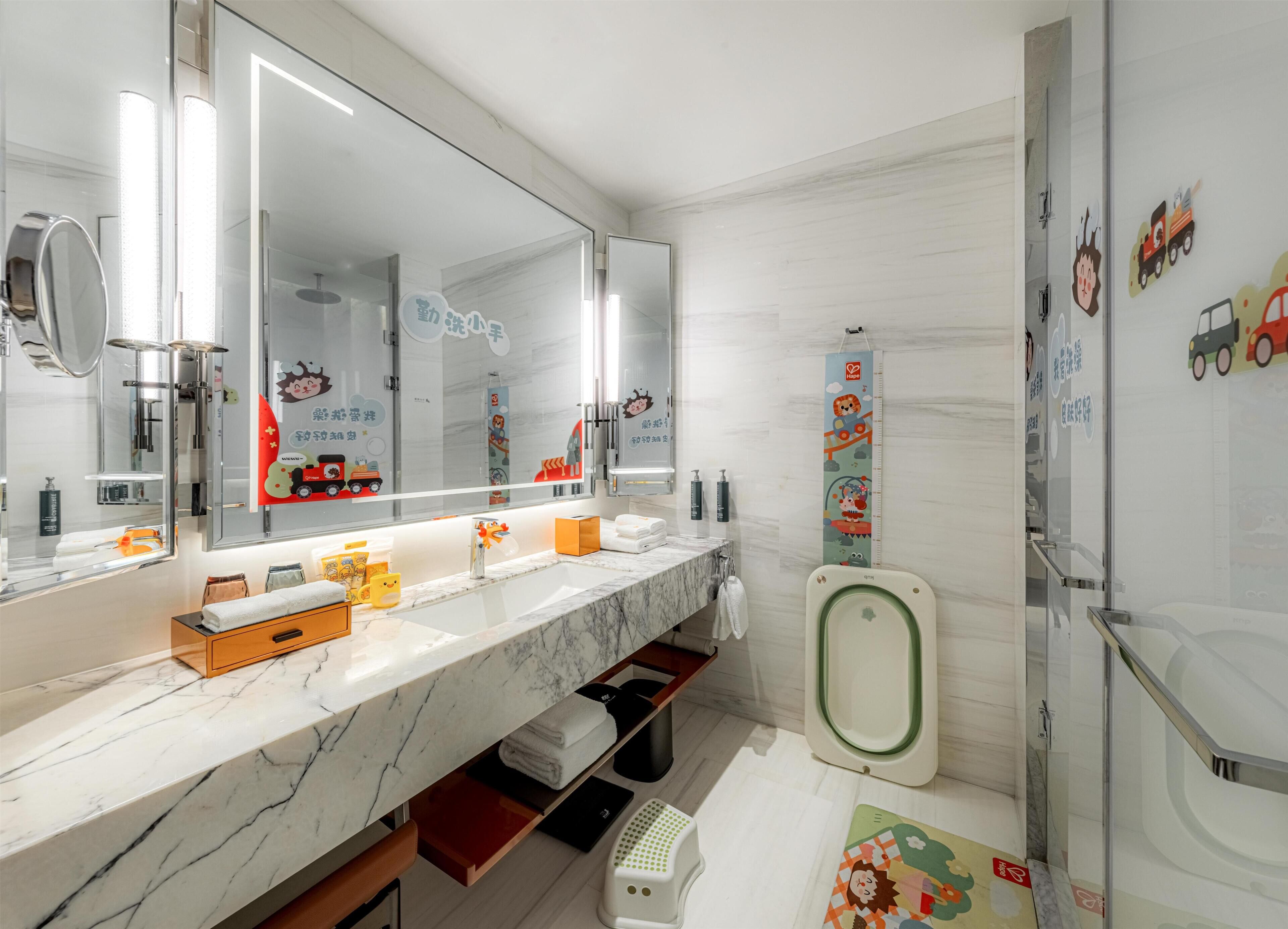 A modern bathroom with a marble vanity, a large mirror, a toilet with a green seat, and children's wall decals.