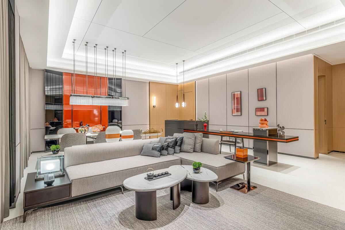 A modern living room with a sectional sofa, two coffee tables, a dining area with a long table, and a kitchen area.