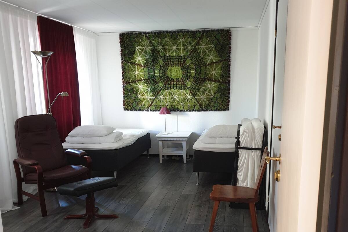 Een kamer met twee bedden, een bureau, een stoel en een groot wandtapijt.