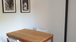 Ein kleiner Raum mit einem Holztisch, weißen Stühlen, zwei gerahmten Bildern an der Wand und einer Tür.