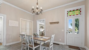 Ein Essbereich mit Holztisch, weißen Stühlen, einer Chandelüster und einer Tür mit bleiverglastem Fenster.