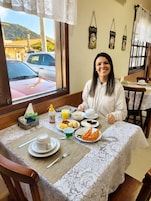 Una mesa de comedor con alimentos para el desayuno, una ventana con vista a un coche estacionado y edificios, y una pared decorada con motivos de café.