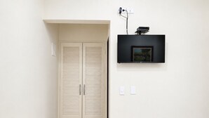 A hallway with a beige double closet, a mounted flat-screen TV, and tiled flooring. - Hotel Pousada Garoupas (São Sebastião)