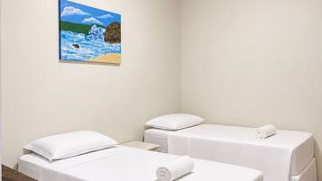 Een hotelkamer met twee bedden, een schilderij van een strand en een kleine tafel.