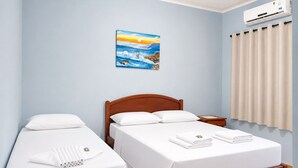 Une chambre d’hôtel avec deux lits, un tableau au mur, un climatiseur et une fenêtre avec des rideaux.