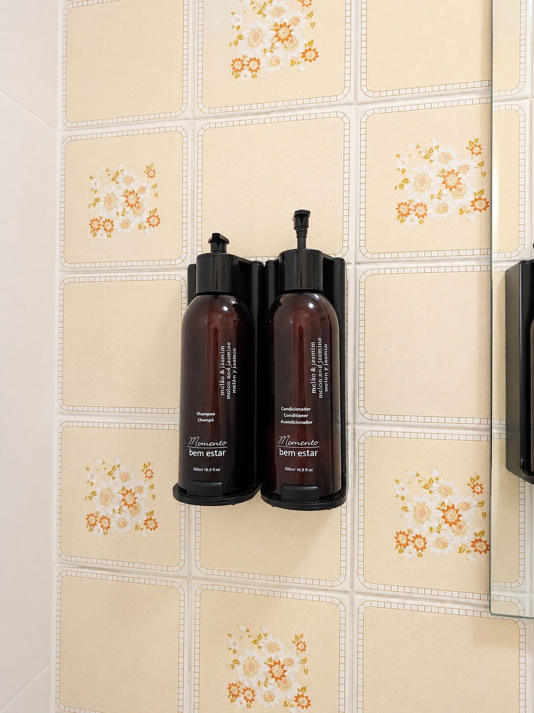 Two bottles of shampoo and conditioner on a tiled wall.