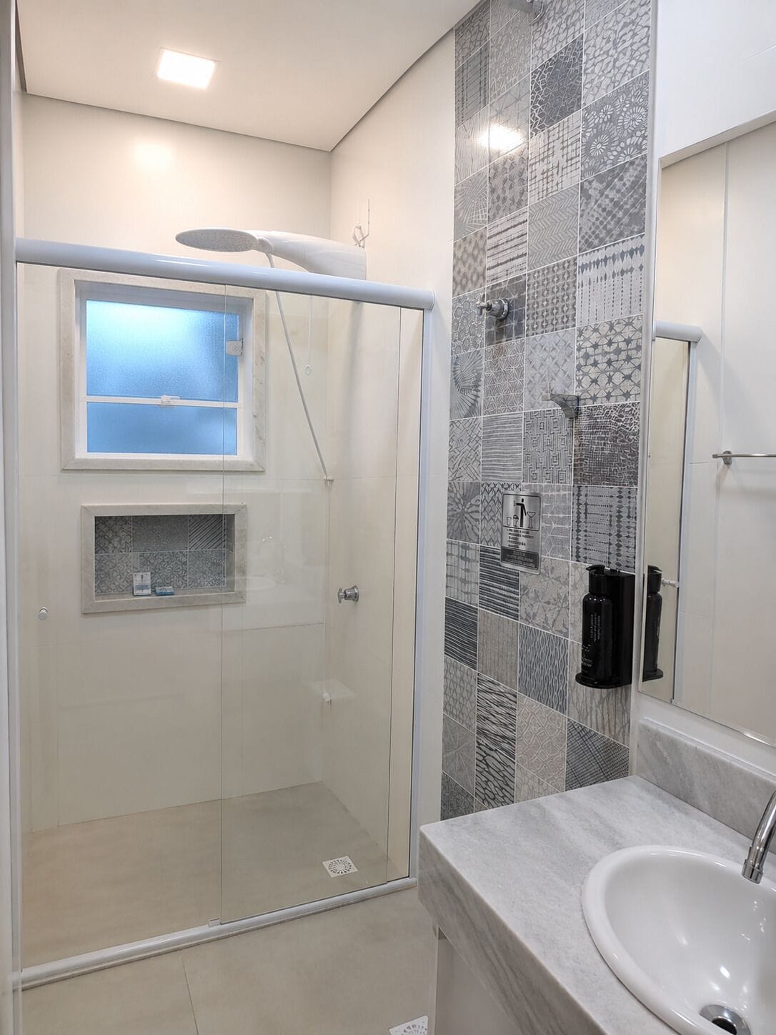 Uma casa de banho moderna com cabine de duche em vidro, lavatório e azulejos estampados nas paredes.
