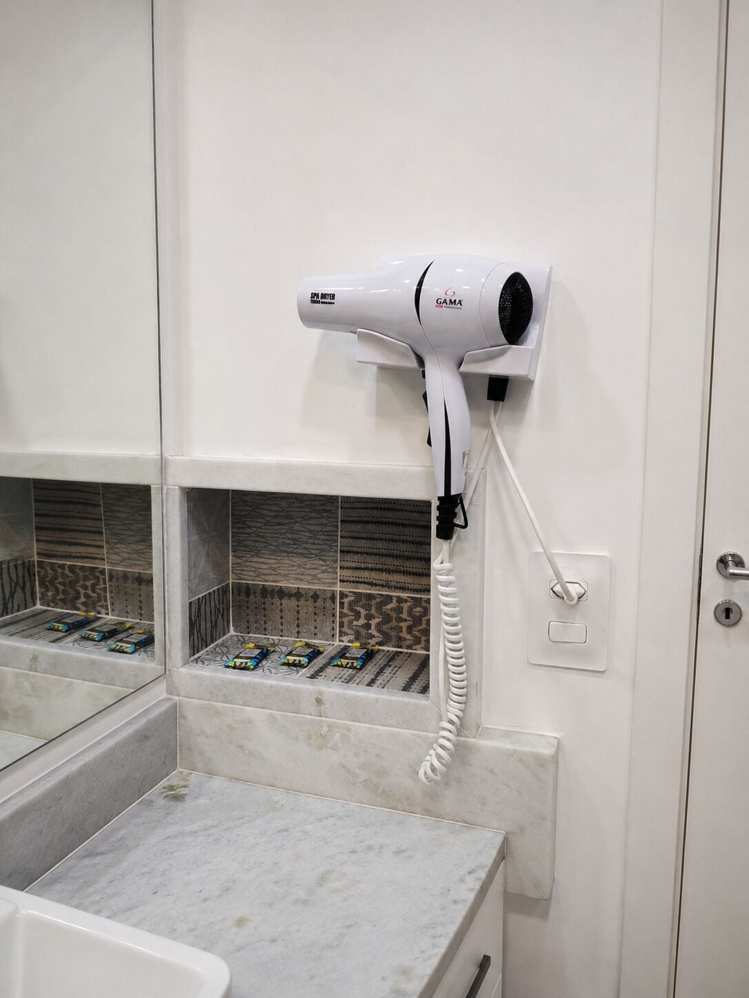A hair dryer mounted on a wall in a bathroom with tiled flooring and a marble countertop.