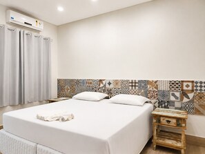 A hotel room with a large bed, a bedside table with a drawer, a wall-mounted air conditioner, and a patterned tile backsplash. - Hotel Pousada Garoupas (São Sebastião)