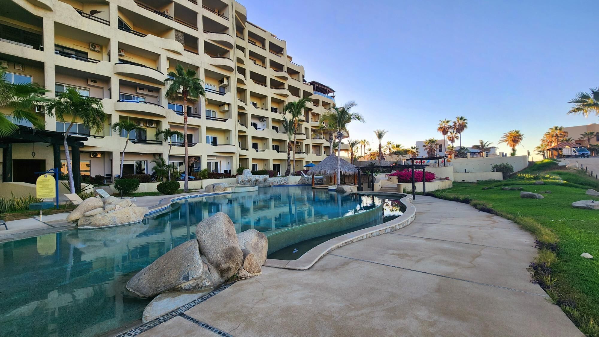 A hotel with a large pool, palm trees, and a multi-story building.