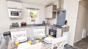 A modern kitchen with white cabinetry, a built-in microwave, a gas stove, and a window overlooking a garden. - Honeysuckle Lodge (Saltburn-by-the-Sea)