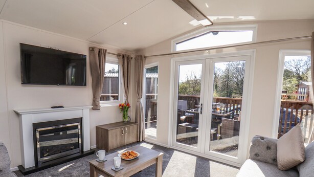 A living room with a fireplace, a flat-screen TV, a sofa, a coffee table, and a balcony with outdoor furniture. - Honeysuckle Lodge (Saltburn-by-the-Sea)