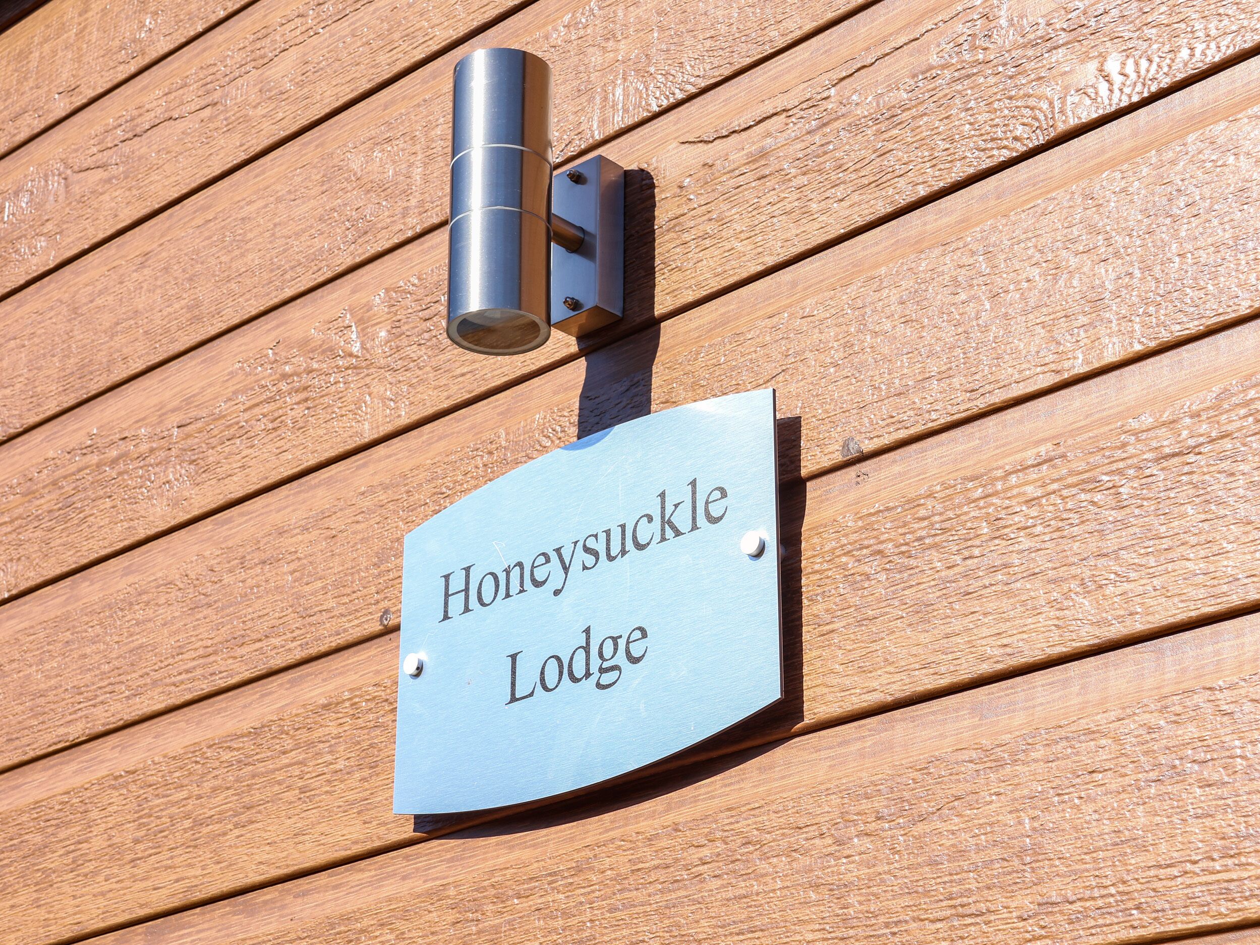 A metal sign with the text "Honeysuckle Lodge" mounted on a wooden wall.