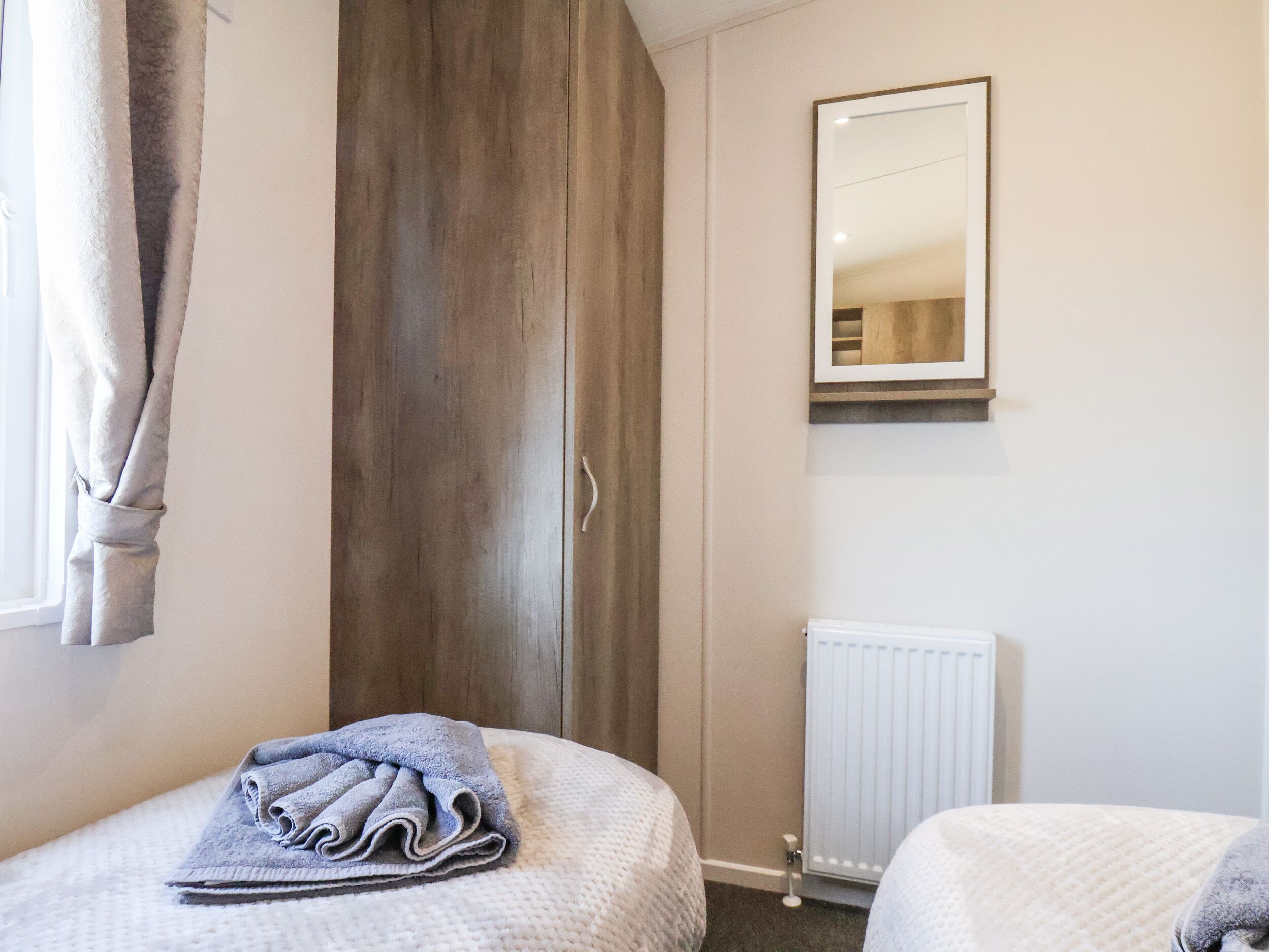 Een slaapkamer met twee bedden, een houten garderobe, een radiator en een spiegel aan de muur.