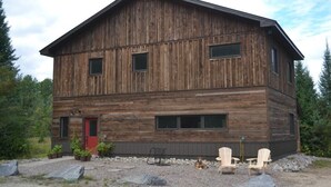 A two-story wooden cabin with a red door, large windows, and a gravel driveway. - Country Cottage on 80 acres (Burk's Falls)