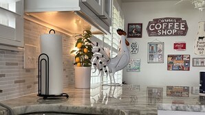 Een keuken met een marmeren aanrecht, een spoelbak, een keukenpapierdispenser, een decoratieve haan, en een muur met verschillende borden, waaronder een bord voor een koffietent.