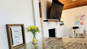 Een keuken met een marmeren aanrecht, een wit bakstenen haard, een lijst met een inspirerende quote, en een vaas met gele bloemen.