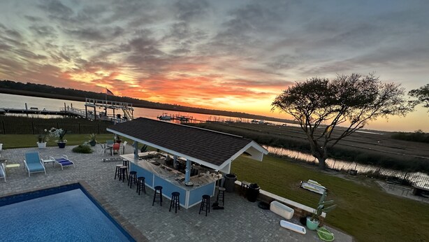 Zwembadgedeelte met ligbedden en een bar, met uitzicht op een waterpartij bij zonsondergang.