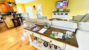 A living room with a wooden coffee table, a sofa, and a TV mounted on the wall. - Bourbon Trail POOL Zone! HotTub! PoolTable! PingPong! GoldenTee! BigYard! PETS! (Springfield)