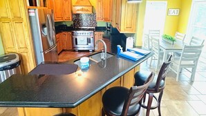 A kitchen with wooden cabinets, a stainless steel refrigerator, a stove, and a large island with bar stools. - Bourbon Trail POOL Zone! HotTub! PoolTable! PingPong! GoldenTee! BigYard! PETS! (Springfield)
