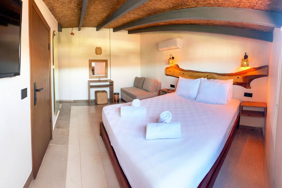 A hotel room with a large bed, a wooden headboard, a bedside table, a nightstand, a small seating area with a sofa, a chair, and a wall-mounted mirror.