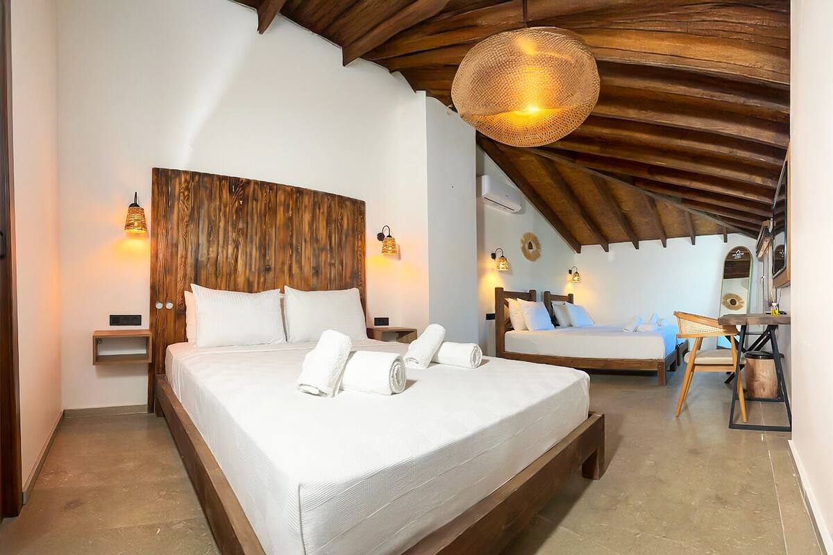 A bedroom with a large bed, a smaller bed, and a desk with a chair. There are wall-mounted lights and a hanging light fixture.