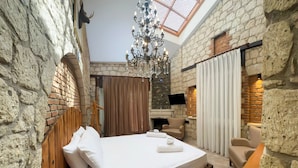 A bedroom with a large bed, a chandelier, a fireplace, and stone walls. - Nuriye Alacati (Cesme)