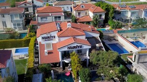 A large house with a red-tiled roof, a swimming pool, and a sign that reads "NURIYE ALAGATI". - Nuriye Alacati (Cesme)