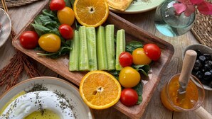 A wooden table with a variety of food items including a plate of vegetables, a bowl of yogurt, and a plate of stuffed peppers. - Nuriye Alacati (Cesme)