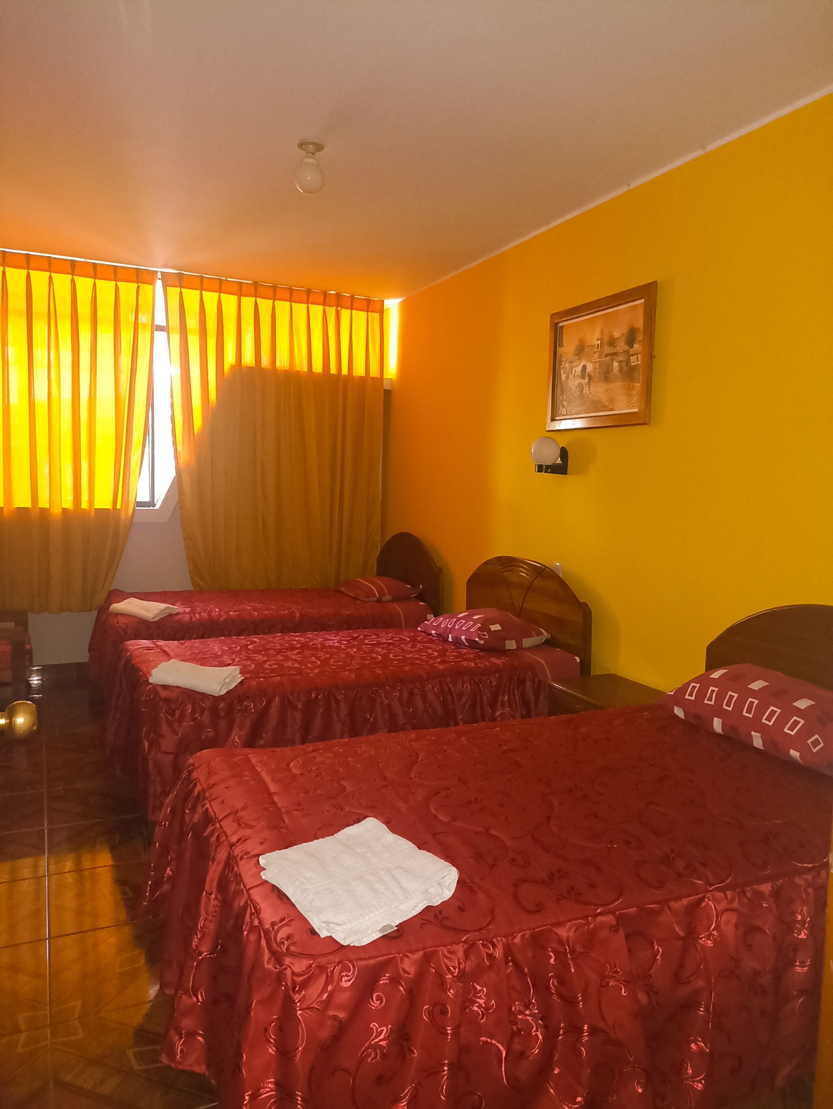 A hotel room with two beds, a wooden floor, and a window with yellow curtains.