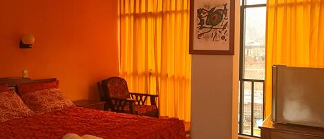 Una habitación de hotel con cama, sillón, televisor y ventana con cortinas.