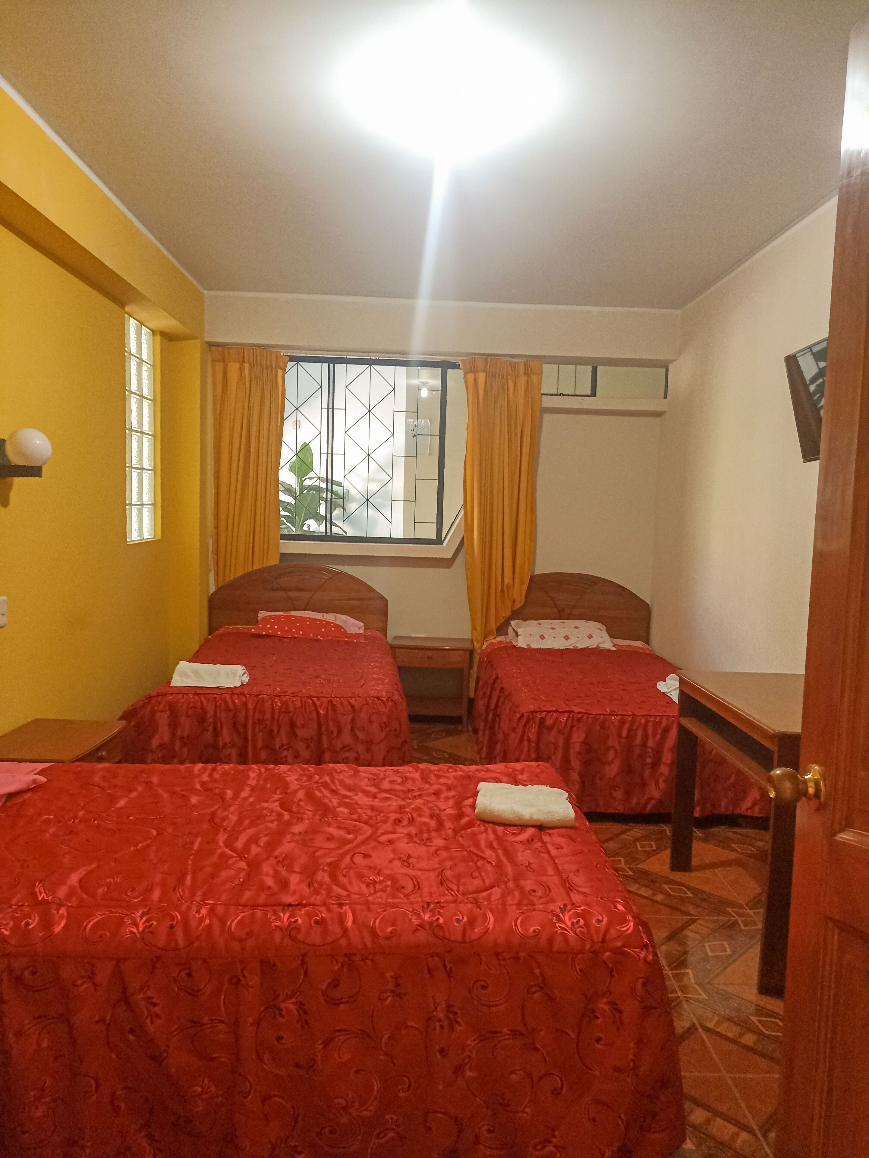 Una habitación con cuatro camas individuales, una ventana con cortinas amarillas y vistas a zonas verdes.