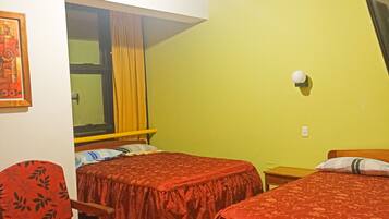 Une chambre avec deux lits, une chaise, une fenêtre avec des rideaux et un luminaire fixé au mur.