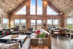 A spacious room with high ceilings and large windows, a cozy seating area with a sofa and chairs, and a dining table set for a meal.