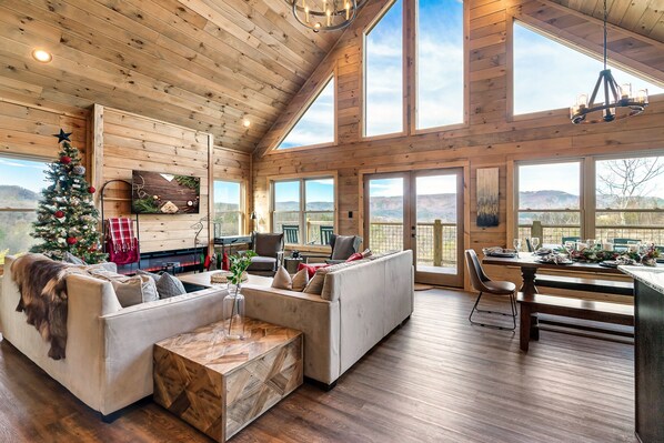 A spacious living room with a fireplace, a Christmas tree, and a dining area with a view of the mountains.