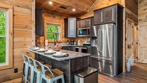 A modern kitchen with wooden walls, stainless steel appliances, and a central island with bar stools. - Mtn Cabin · Hot Tub · Game Room · Fire Pit (Sevierville)