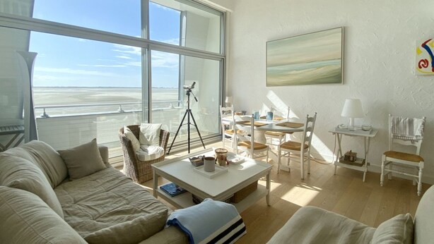 A spacious living room with a large window, a white sofa, a coffee table, and a dining area with chairs and a table. - Les Pieds dans l'Eau, bay view for 6 people (Le Crotoy)