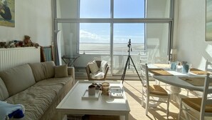 A room with a large window, a sofa, a table with items, a chair, and a tripod. - Les Pieds dans l'Eau, bay view for 6 people (Le Crotoy)