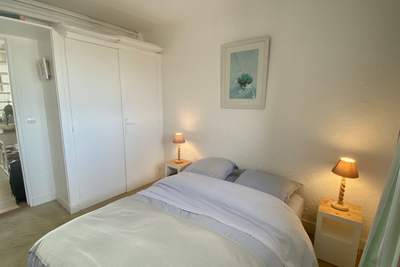 Une chambre à coucher avec un lit, deux tables de chevet avec des lampes, une armoire et un tableau encadré au mur.
