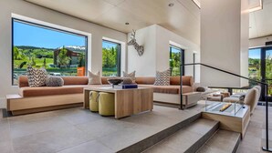 A modern living room with a large window, a fireplace, and a staircase leading to an upper level. - Electric Pass Lodge (Snowmass Village)