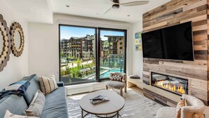 A modern living room with a sofa, a coffee table, a fireplace, and a large TV. - Electric Pass Lodge (Snowmass Village)