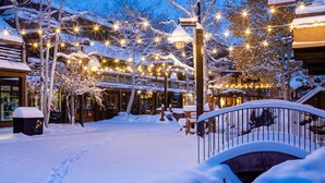 A snow-covered outdoor area with a bridge, trees, and string lights. - Electric Pass Lodge (Snowmass Village)