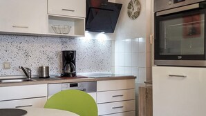 A modern kitchen with white cabinetry, a coffee maker, a microwave, and a clock on the wall. - 1 bedroom cozy apartment in Börgerende (Börgerende)
