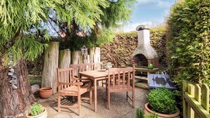 A wooden outdoor seating area with a stone oven, surrounded by potted plants and a wooden fence. - 1 bedroom cozy apartment in Börgerende (Börgerende)