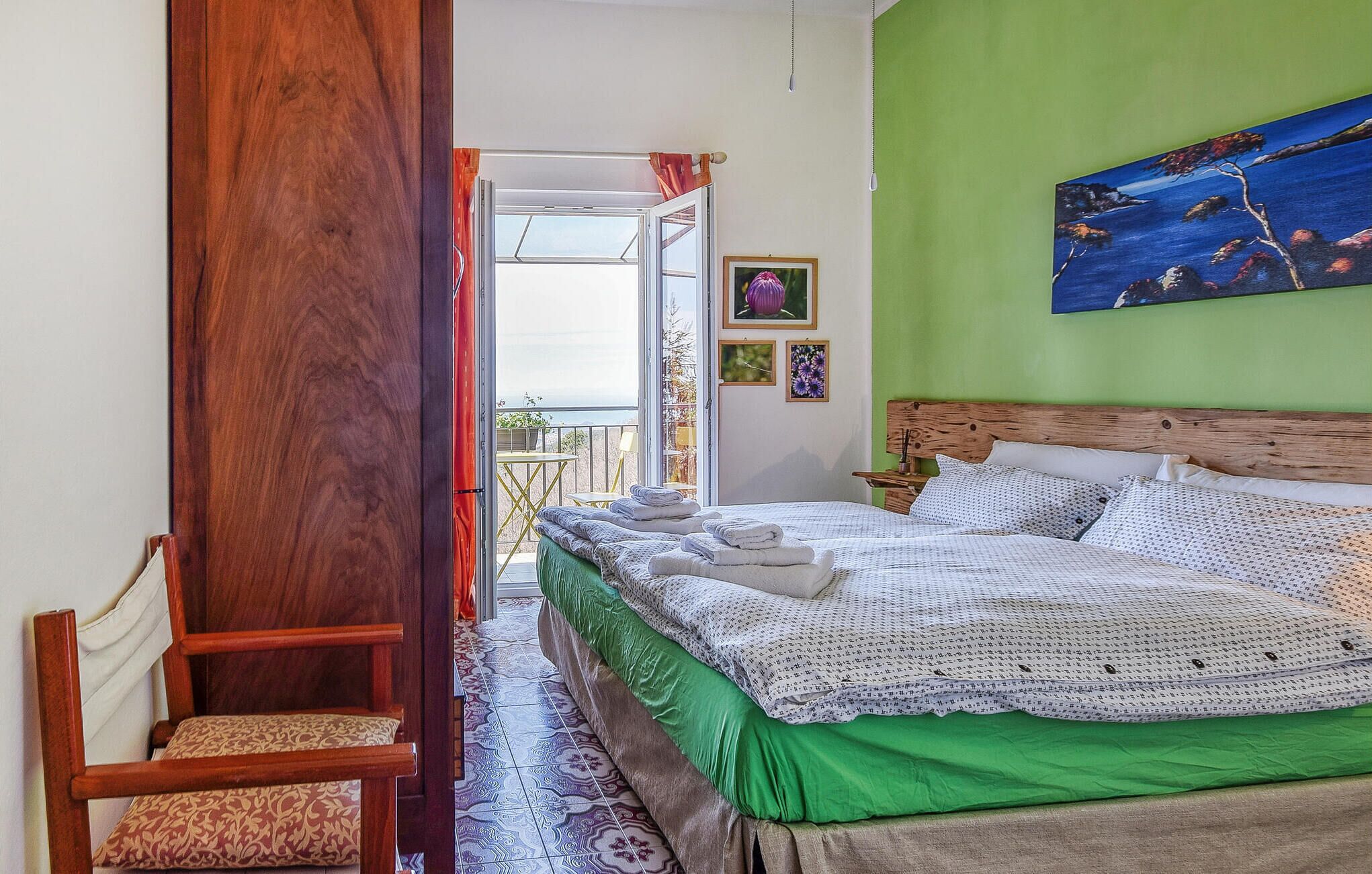 Een slaapkamer met een houten hoofdeinde, een bed met wit en gemêleerd beddengoed, een groene accentmuur en een schilderij boven het bed.