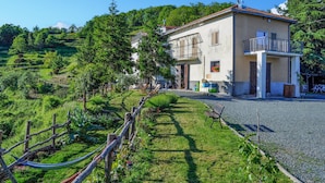 A two-story building with a balcony, surrounded by a well-maintained garden and a hilly landscape.